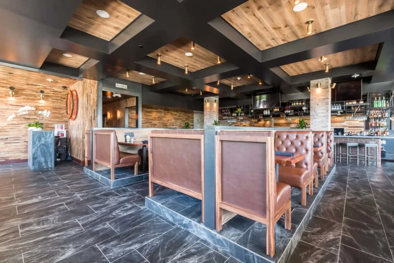 Raised leather booths under a coffered wood ceiling leading back to the bar at Tap 42 Aventura