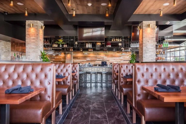 Tufted leather booths with folded napkins framing a view of the bar and TVs at Tap 42 Aventura