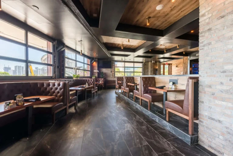 Window-lined row of tufted booths beside a whitewashed brick column at Tap 42 Aventura