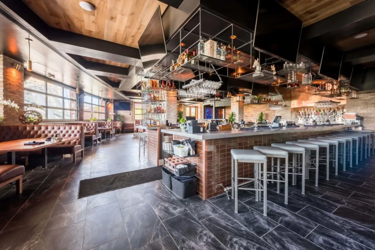Wide view of the copper-tiled bar, white stools and booths along the windows at Tap 42 Aventura