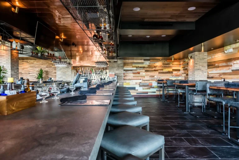 Bar counter set with glassware and gray stools beside high-tops and a reclaimed wood wall at Tap 42 Aventura