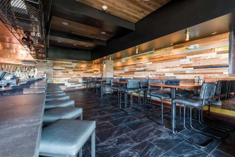 High-top tables with gray chairs along a colorful reclaimed wood wall next to the bar at Tap 42 Aventura