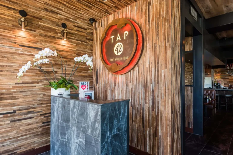 Marble host stand with white orchids below the glowing red-edged logo sign at Tap 42 Aventura