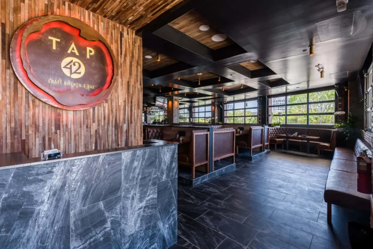 Host stand and logo sign looking into the dining room's booths and garage-style windows at Tap 42 Aventura