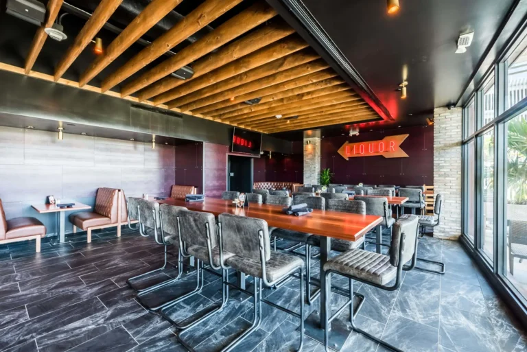Long communal high-top under exposed wood beams with a neon liquor sign beyond at Tap 42 Aventura