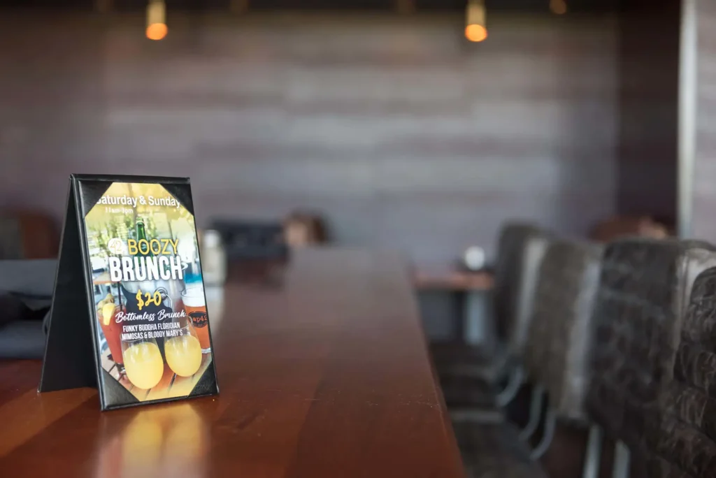 Boozy brunch table card advertising bottomless mimosas on a wood high-top at Tap 42 Aventura