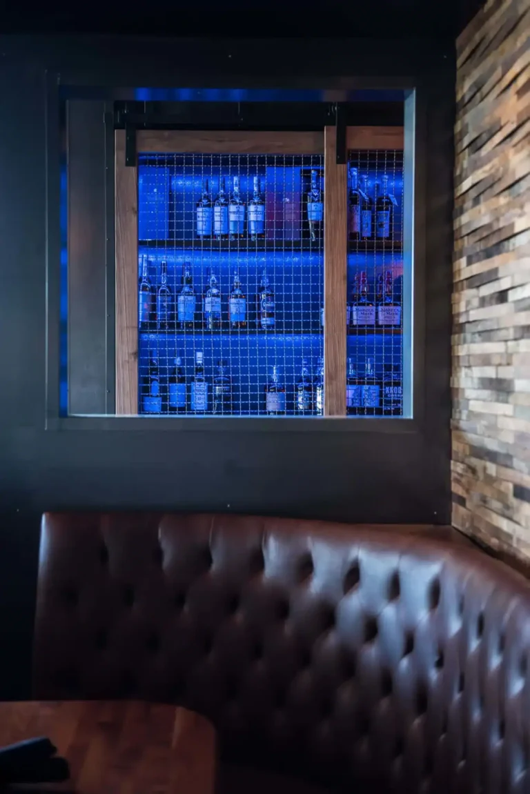 Tufted leather booth beneath a blue-lit window display of liquor bottles behind wire mesh at Tap 42 Aventura