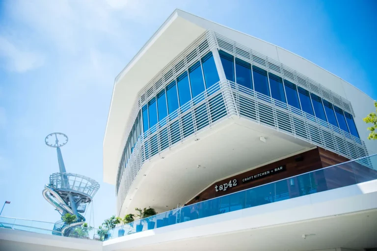 Low-angle view of the modern white building and glass-railed terrace housing Tap 42 Aventura