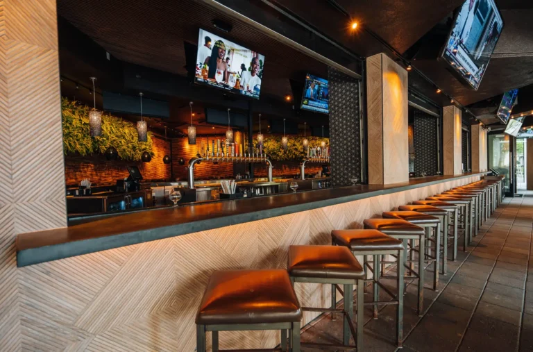 Long herringbone-paneled bar with leather stools, beer taps, a green wall and TVs at Tap 42 Boca Raton