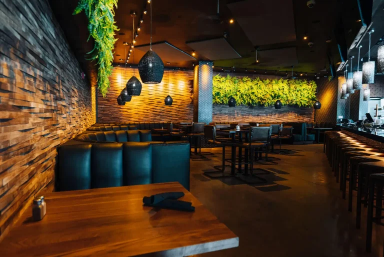 Dark leather booths under black woven pendant lights with a fern green wall and stacked wood walls at Tap 42 Boca Raton
