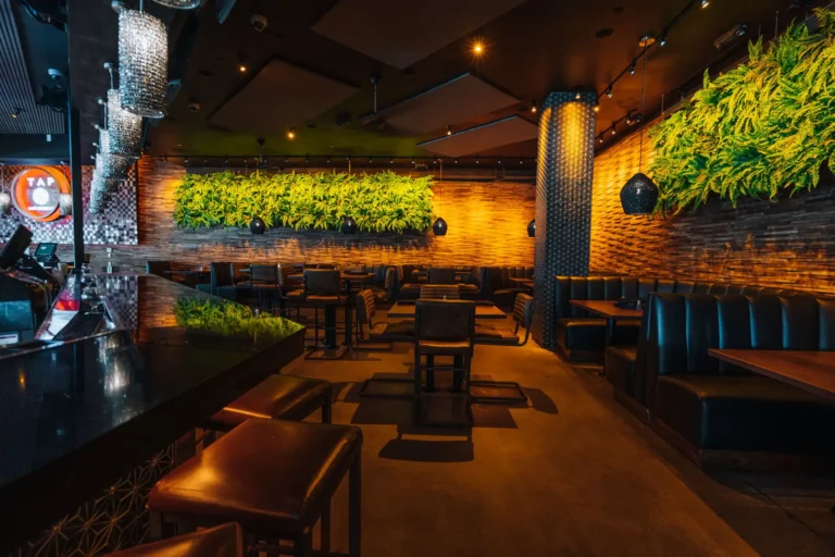 Dining room seen from the bar, with booths, high-tops, fern walls and crystal pendant lights at Tap 42 Boca Raton