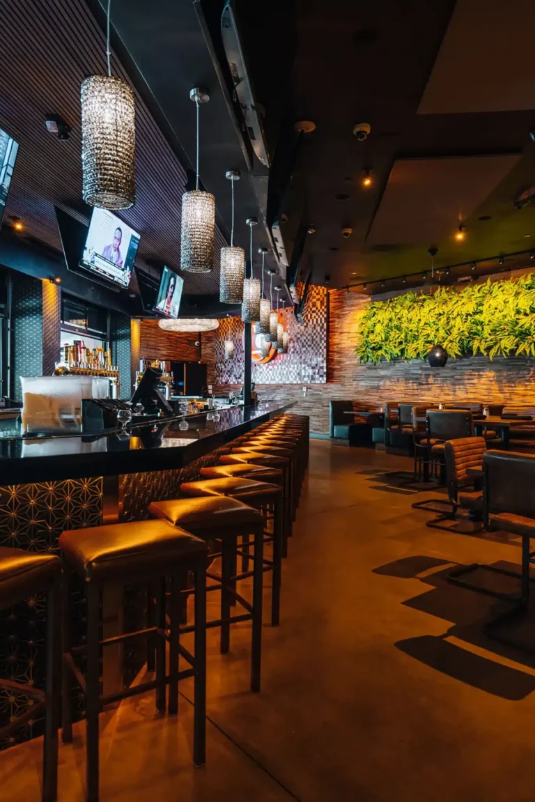 Row of leather bar stools under crystal pendant lights leading toward a fern-covered dining room at Tap 42 Boca Raton