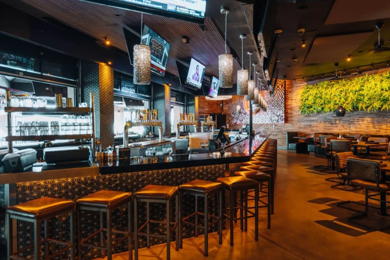 Wide view of the indoor bar with gold leather stools, crystal pendants, TVs and a green wall dining area at Tap 42 Boca Raton