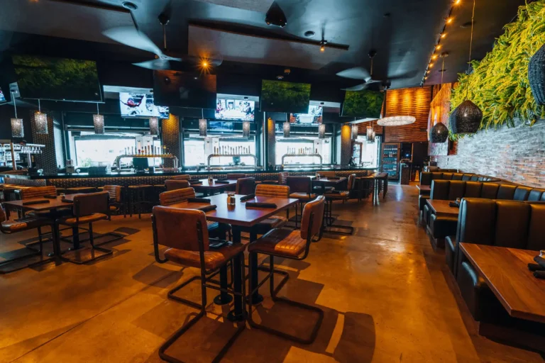 Leather-chair dining tables and booths with a fern wall, ceiling fans and TVs over the window bar at Tap 42 Boca Raton