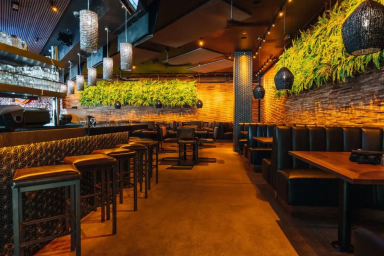 Aisle between gold bar stools and leather booths lit by woven and crystal pendants under fern walls at Tap 42 Boca Raton