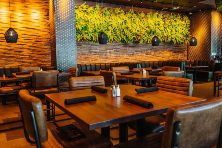 Wood table set with napkins and leather chairs before a glowing fern green wall and black pendants at Tap 42 Boca Raton
