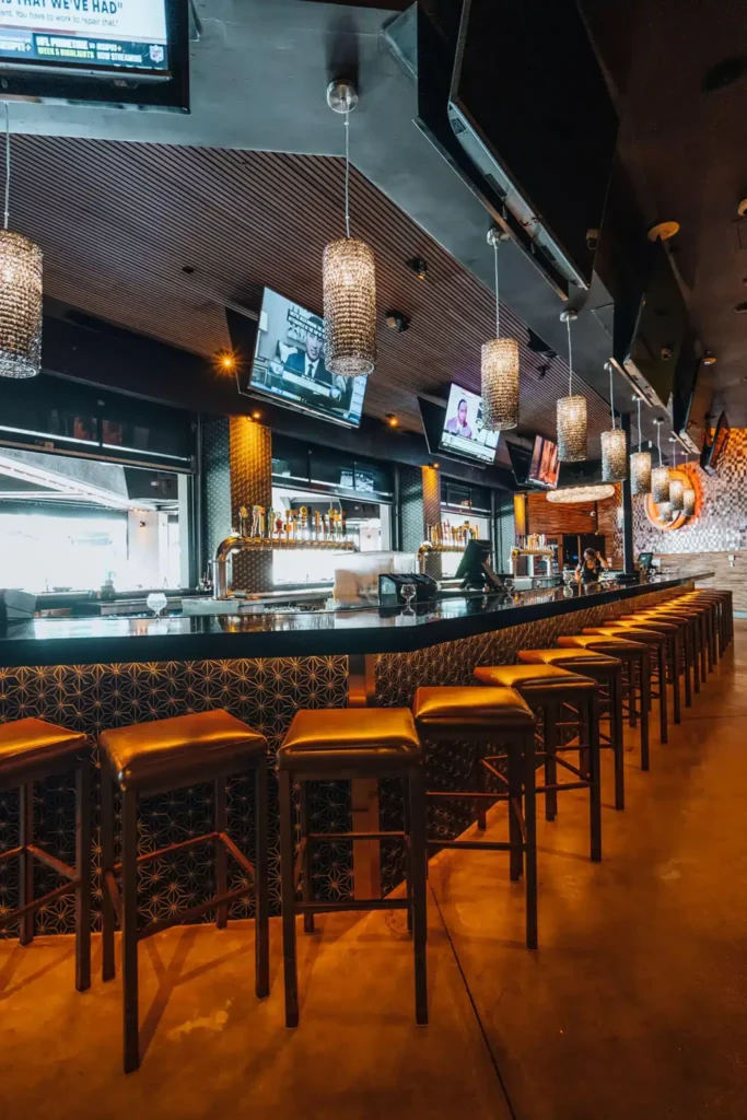 Curving black bar with gold leather stools, crystal pendant lights and TVs in a vertical view at Tap 42 Boca Raton