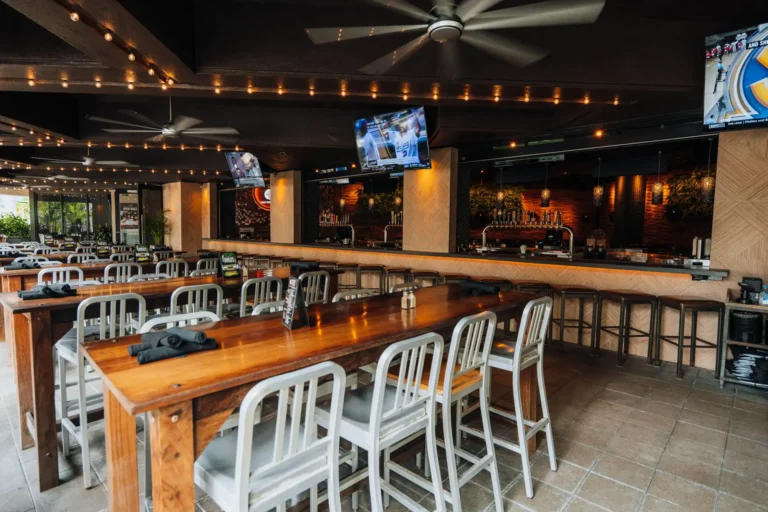 Wide view of patio high-tops and the open-air bar under big ceiling fans, string lights and TVs at Tap 42 Boca Raton