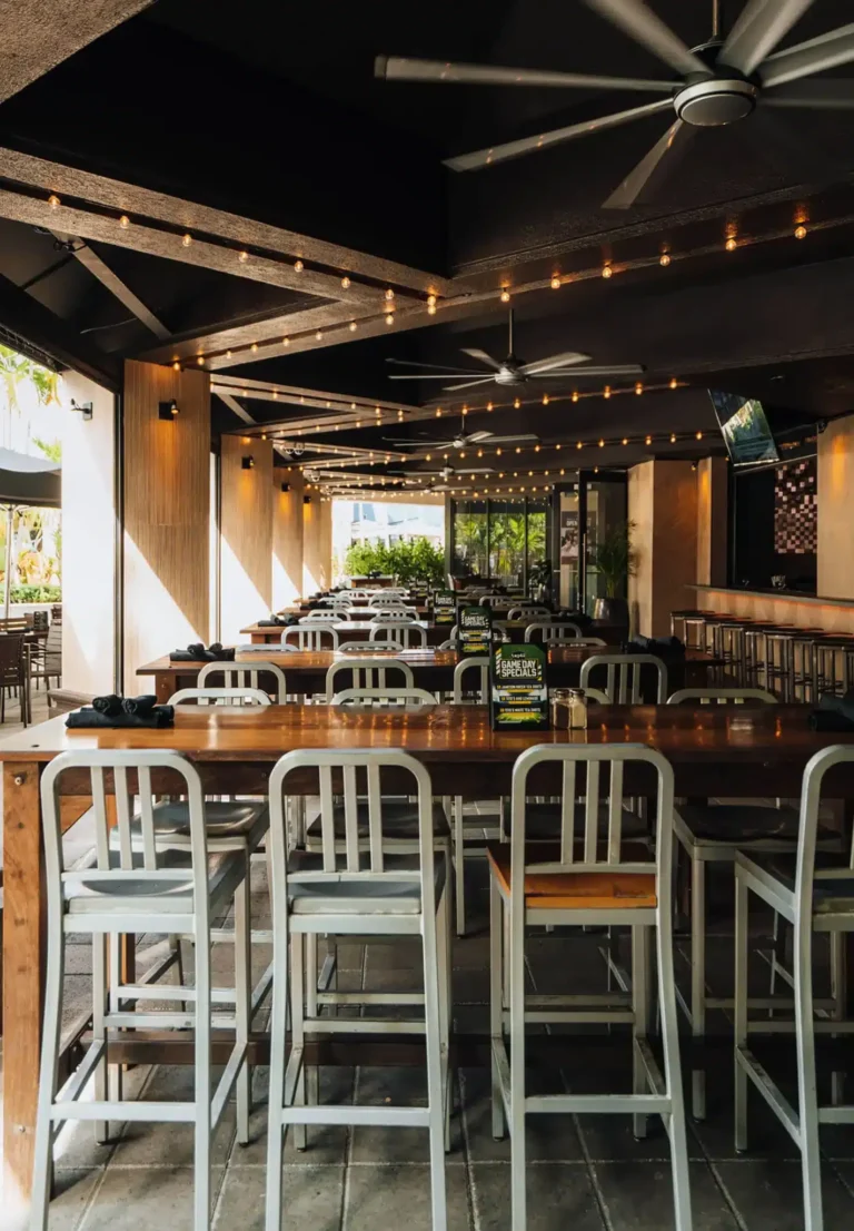 Long rows of aluminum high-top chairs under string lights and ceiling fans in afternoon sun at Tap 42 Boca Raton