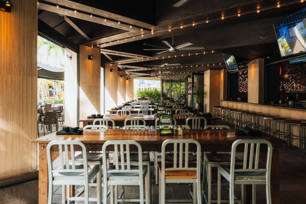 Sunlit covered patio with rows of high-top tables, string lights, ceiling fans and the bar at right at Tap 42 Boca Raton