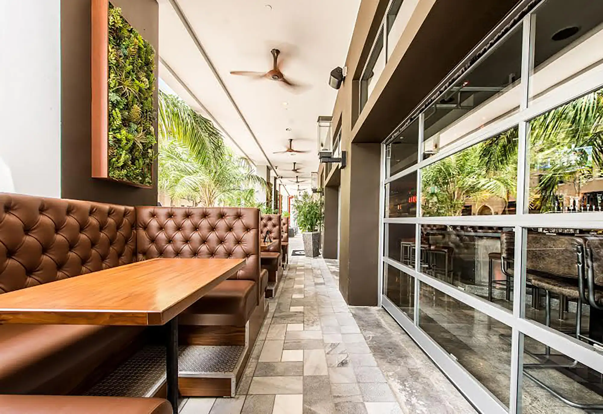 Tufted leather booths on a covered sidewalk patio with a living plant wall and ceiling fans at Tap 42 Coral Gables