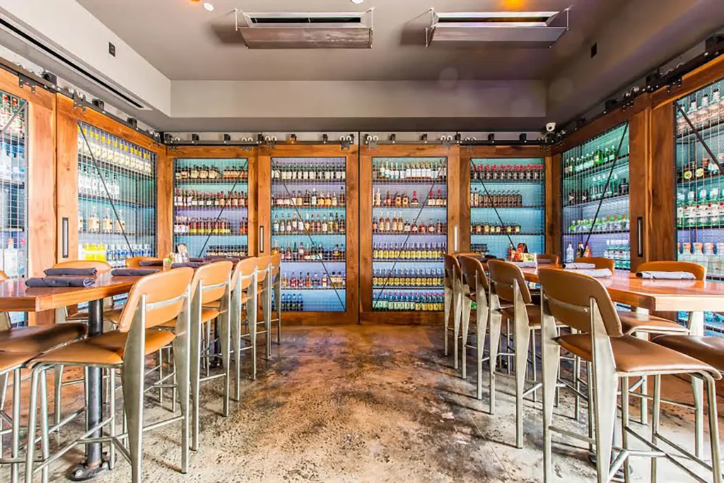 High-top tables before glass-door cabinets stocked with liquor bottles at Tap 42 Coral Gables