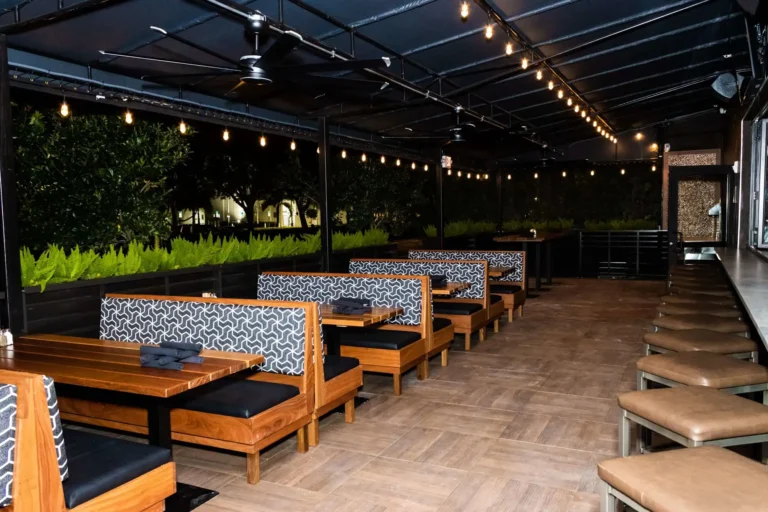 Covered patio at night with string lights, patterned booths, fern planters and bar seating at Tap 42 Coral Springs
