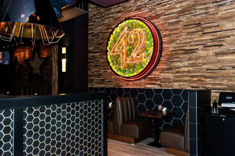 Leather booth for two under a succulent neon 42 sign on a reclaimed wood wall at Tap 42 Coral Springs