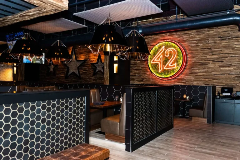 Booths behind black hexagon tile partitions with metal stars and a neon 42 sign at Tap 42 Coral Springs
