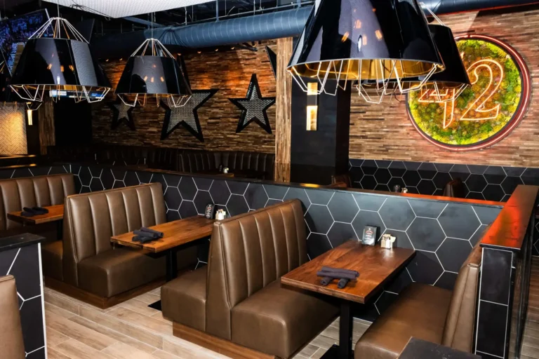 Tufted leather booths with wood tables beneath black pendant lamps and star decor at Tap 42 Coral Springs