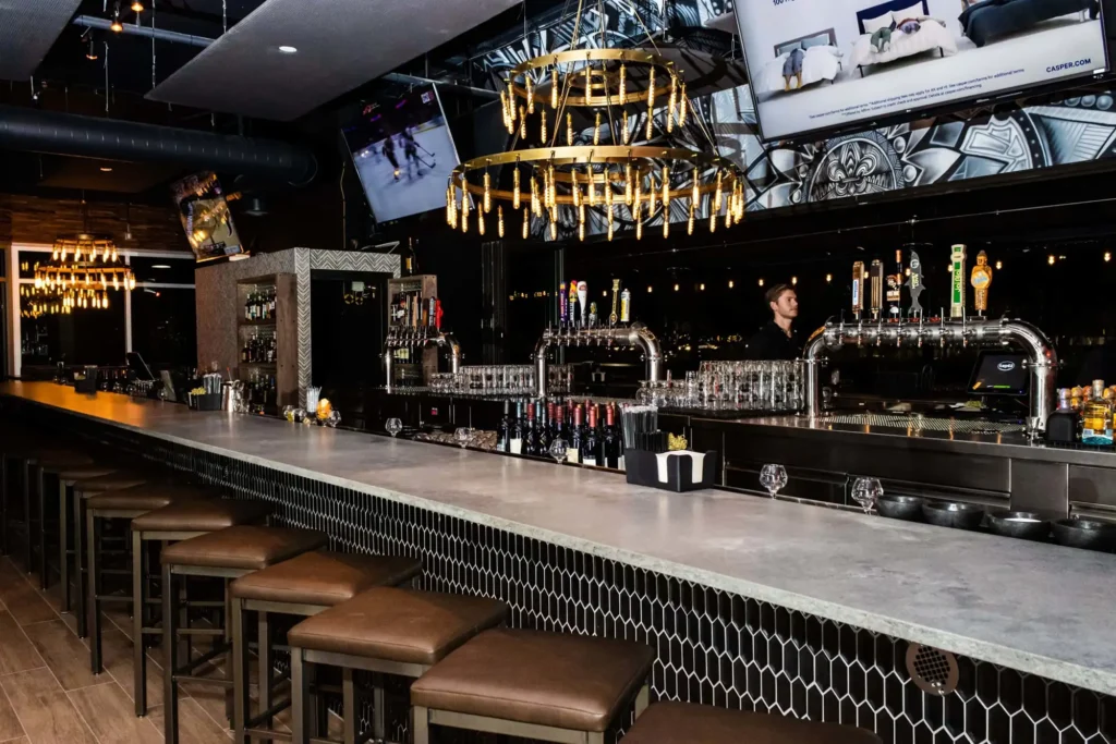 Long concrete bar with leather stools, gold ring chandelier and chrome beer towers at Tap 42 Coral Springs