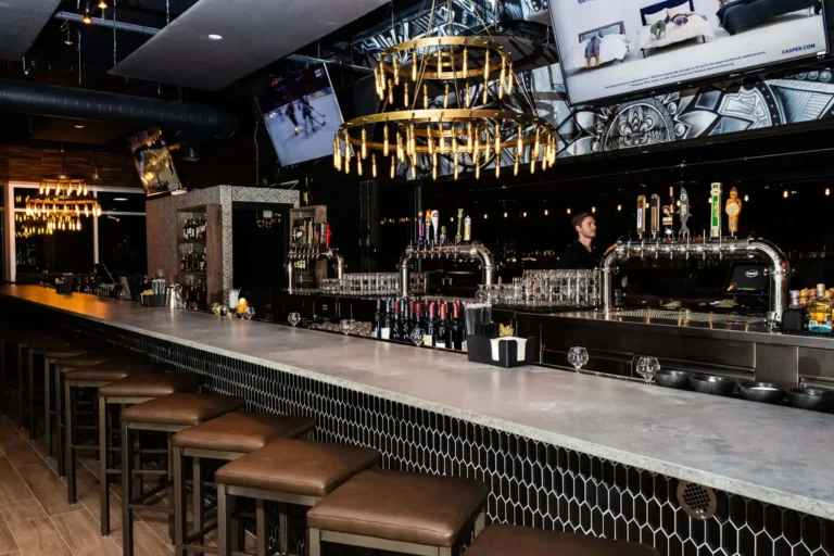 Long concrete bar with leather stools, gold ring chandelier and chrome beer towers at Tap 42 Coral Springs