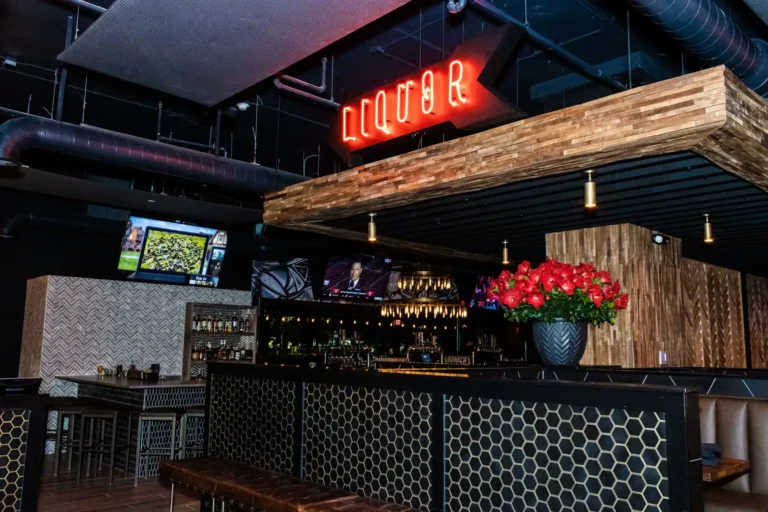 Red neon Liquor sign above the bar area with a vase of red roses and TVs at Tap 42 Coral Springs