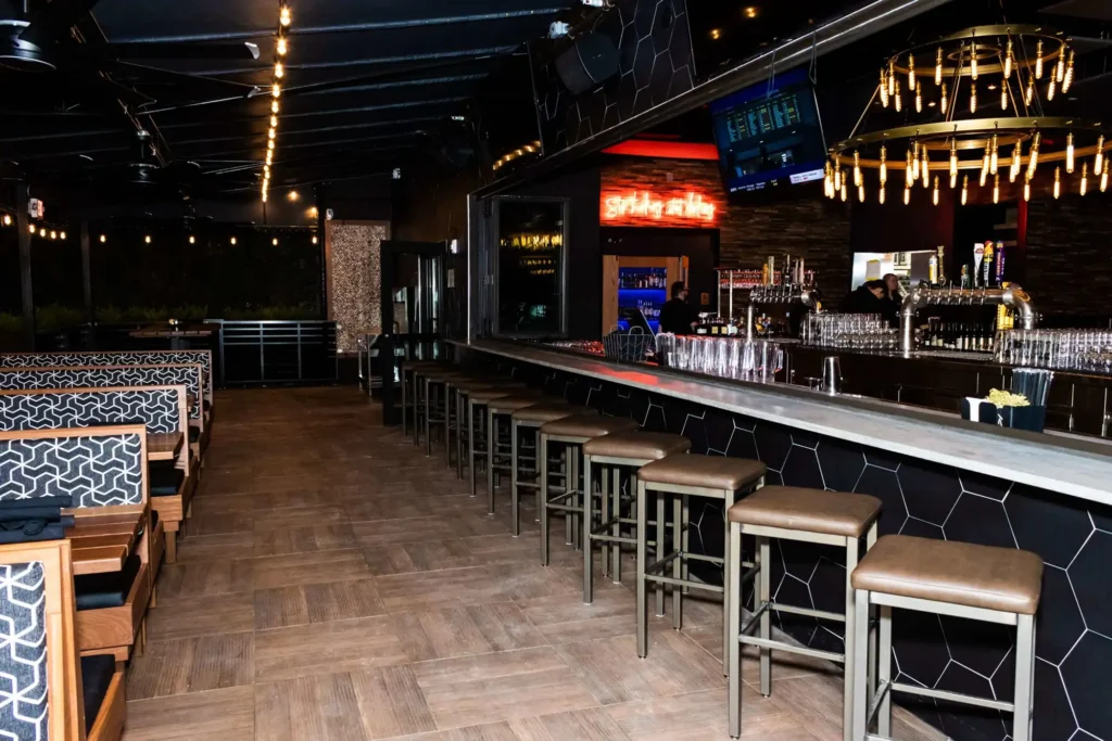 Long bar counter with stools and a ring chandelier opening onto patio booths at Tap 42 Coral Springs
