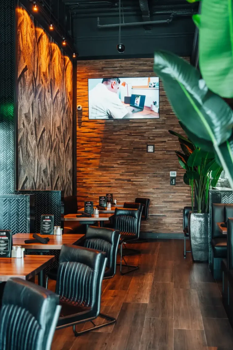 Leather chairs and wood tables beside a carved leaf wall and plank wall with TV at Tap 42 Naples