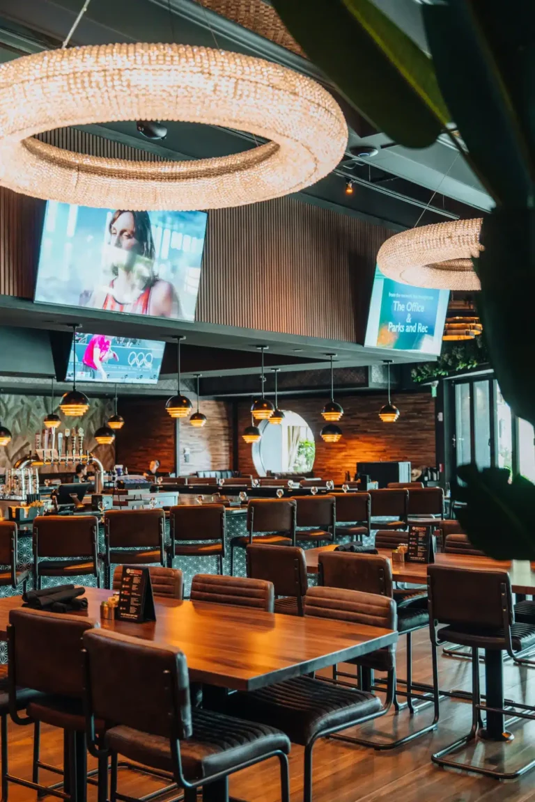 Dining room with crystal ring chandeliers, TVs and long wood tables leading to the bar at Tap 42 Naples