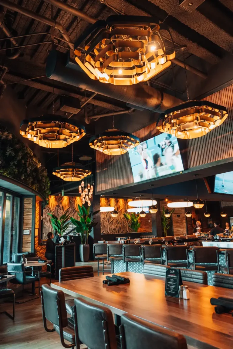 Dining room under glowing gold honeycomb chandeliers, exposed ductwork and TVs at Tap 42 Naples