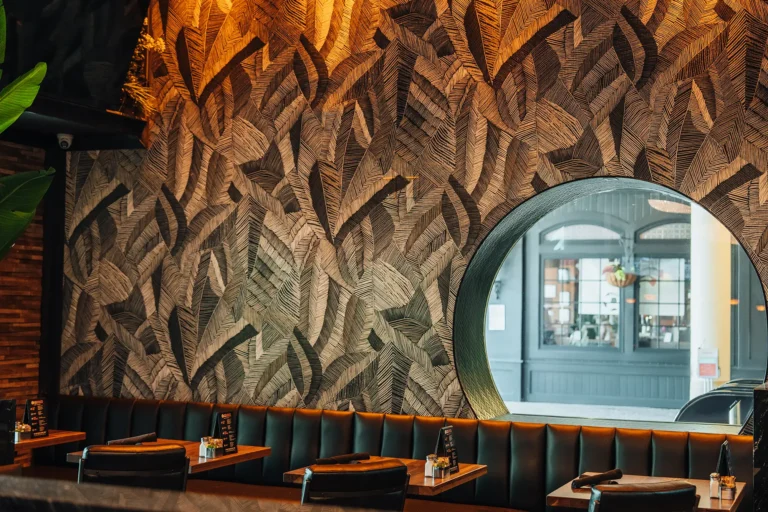Black leather banquette beneath a carved leaf-pattern wall with a round street-view window at Tap 42 Naples