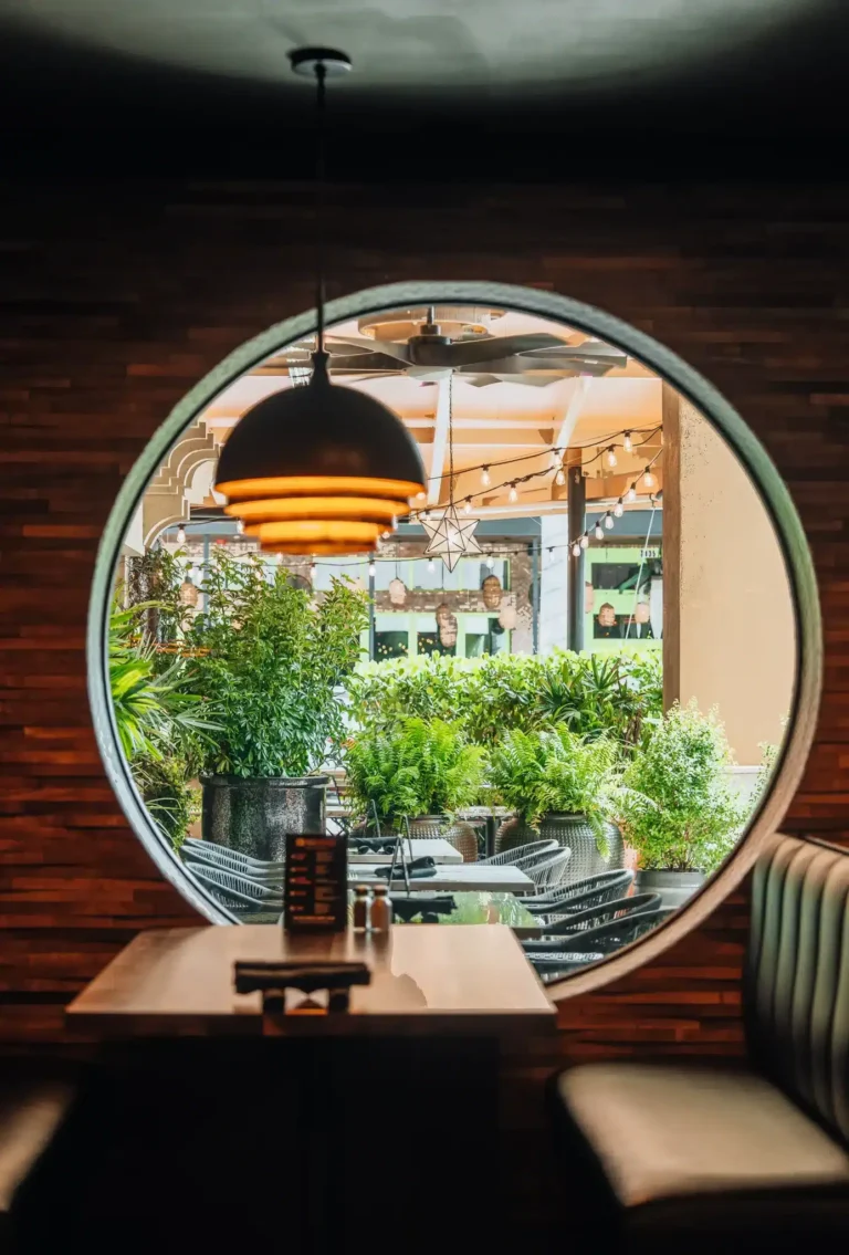Round window framing a patio with potted plants and string lights above a table for two at Tap 42 Naples