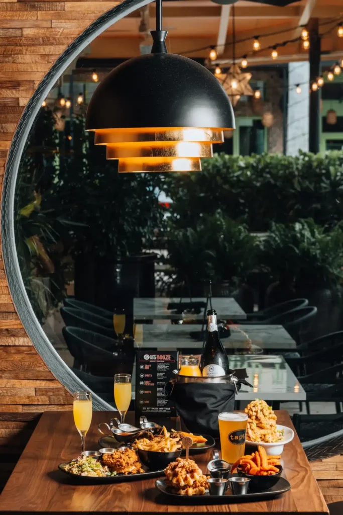 Chicken and waffles, mimosas and a beer under a dome pendant, patio string lights behind, at Tap 42 Naples
