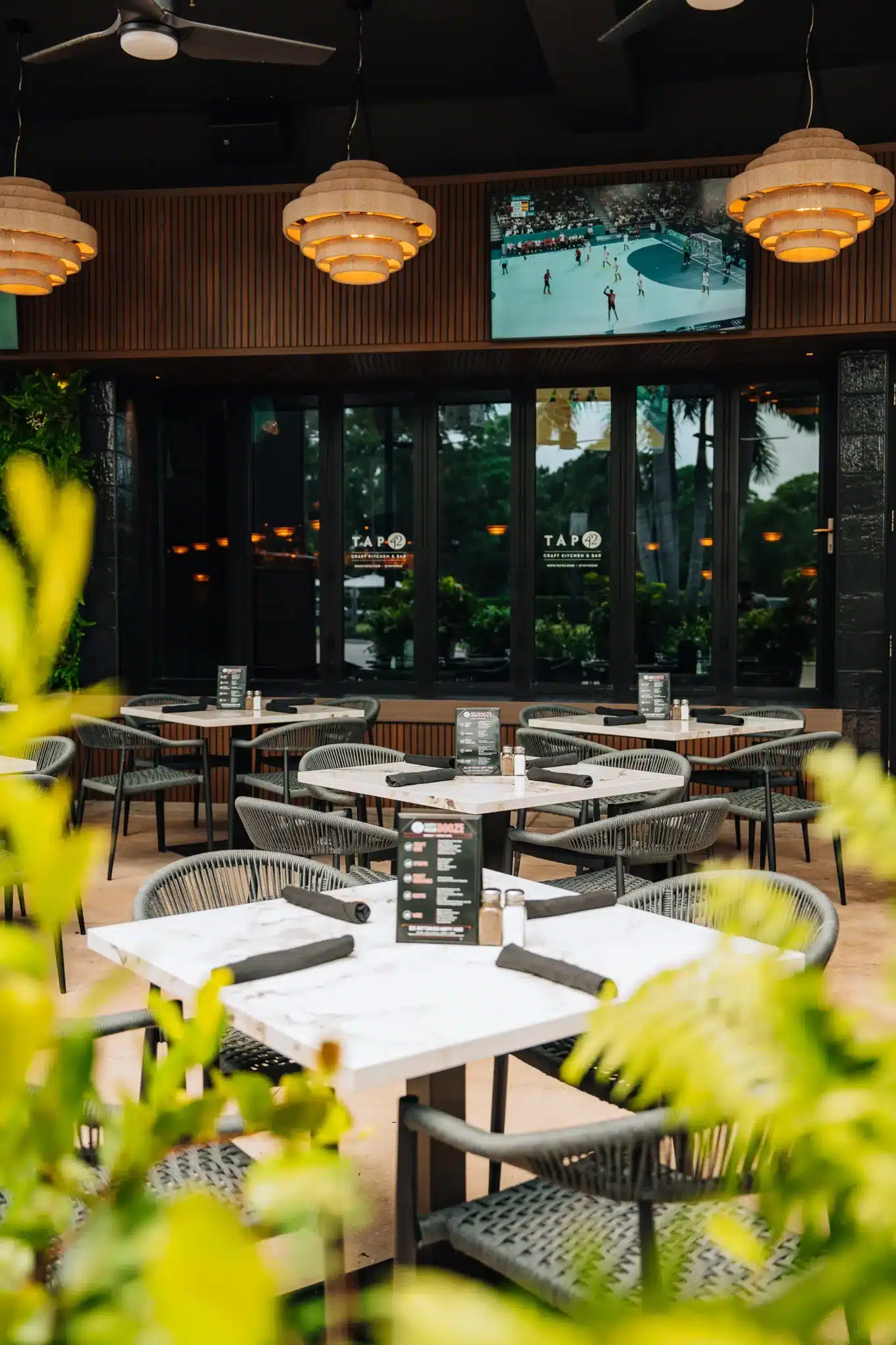 Patio with marble-top tables, woven chairs, wood pendant lights and a TV over glass doors at Tap 42 Naples