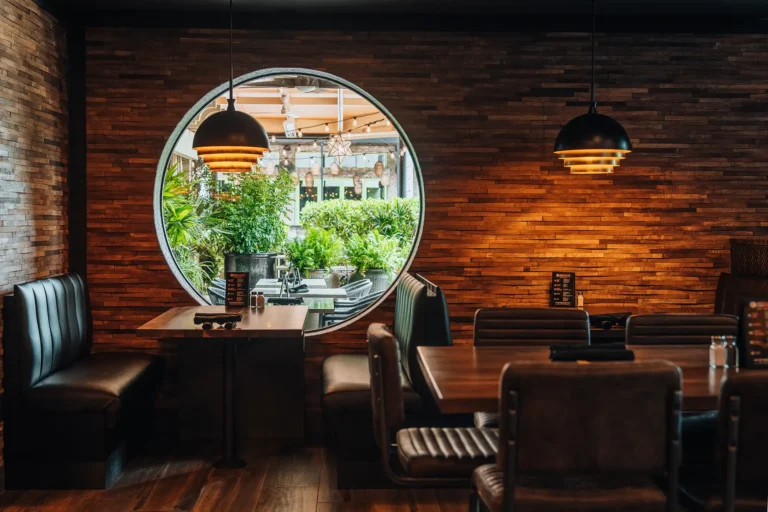 Leather booths and tables beside a round patio window on a wood plank wall with dome pendants at Tap 42 Naples