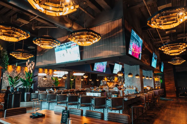Wide view of the bar with high stools, multiple TVs and glowing gold chandeliers at Tap 42 Naples