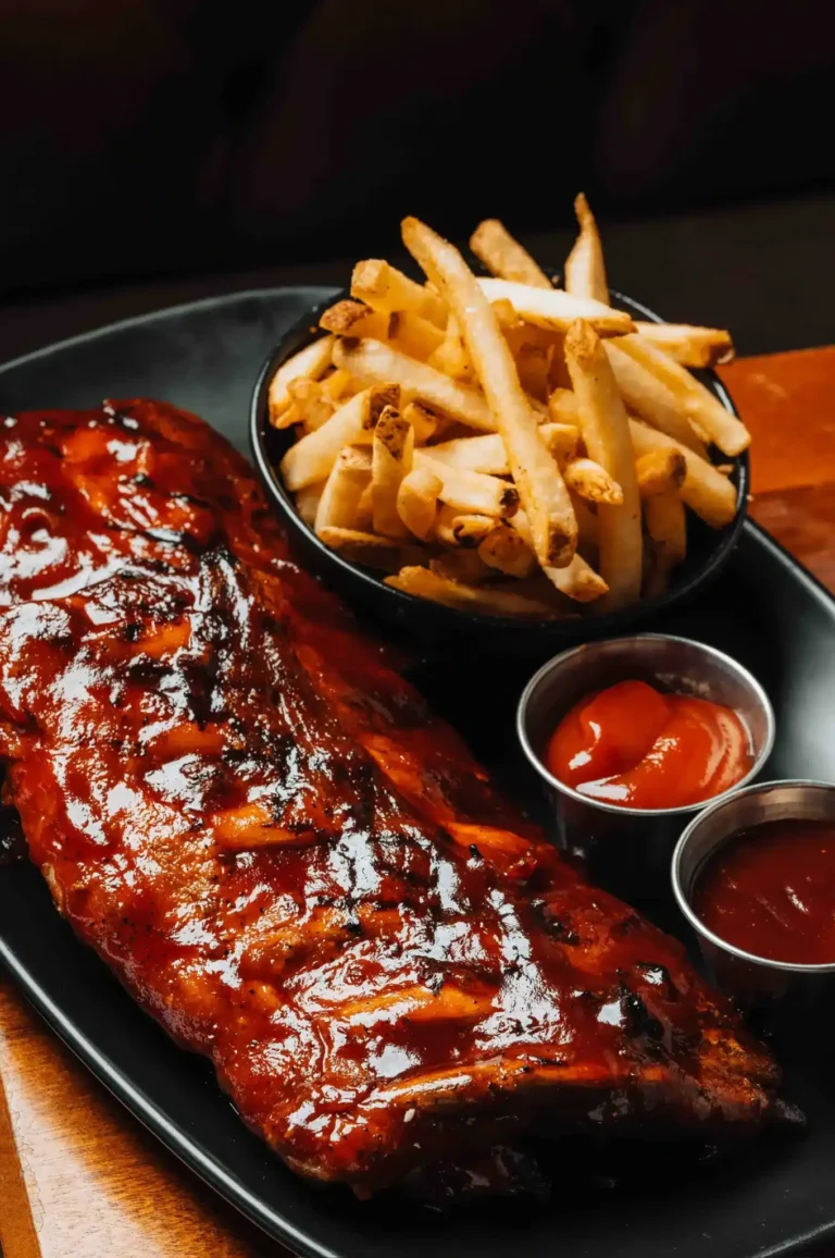 Glazed barbecue ribs with french fries, ketchup and dipping sauce on a black plate at Tap 42 Naples