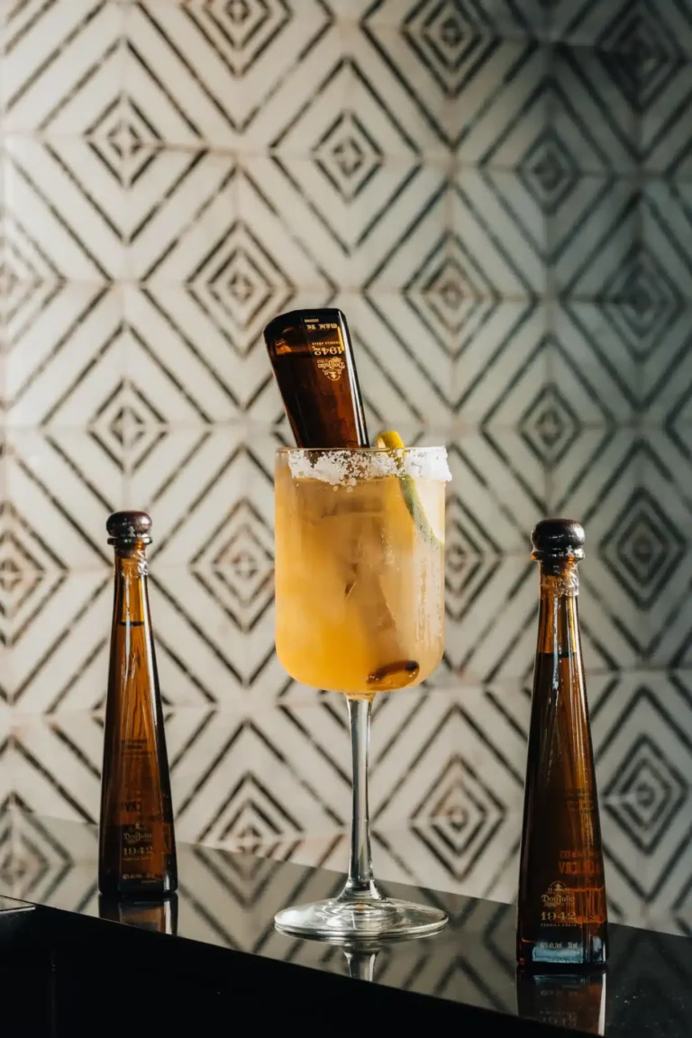 Salt-rimmed cocktail with an upturned mini tequila bottle between two more on patterned tile at Tap 42 Naples
