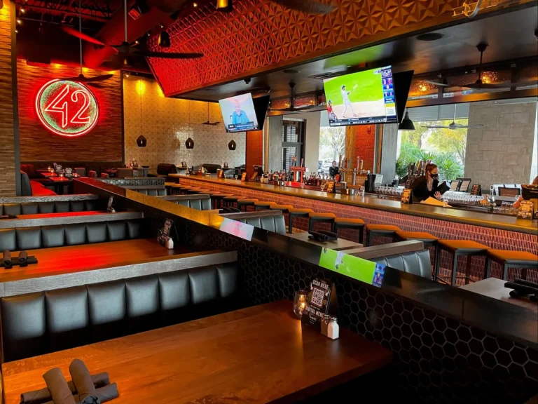Leather booths beside a red neon 42 sign and the bar with TVs under a textured red ceiling at Tap 42 Davie