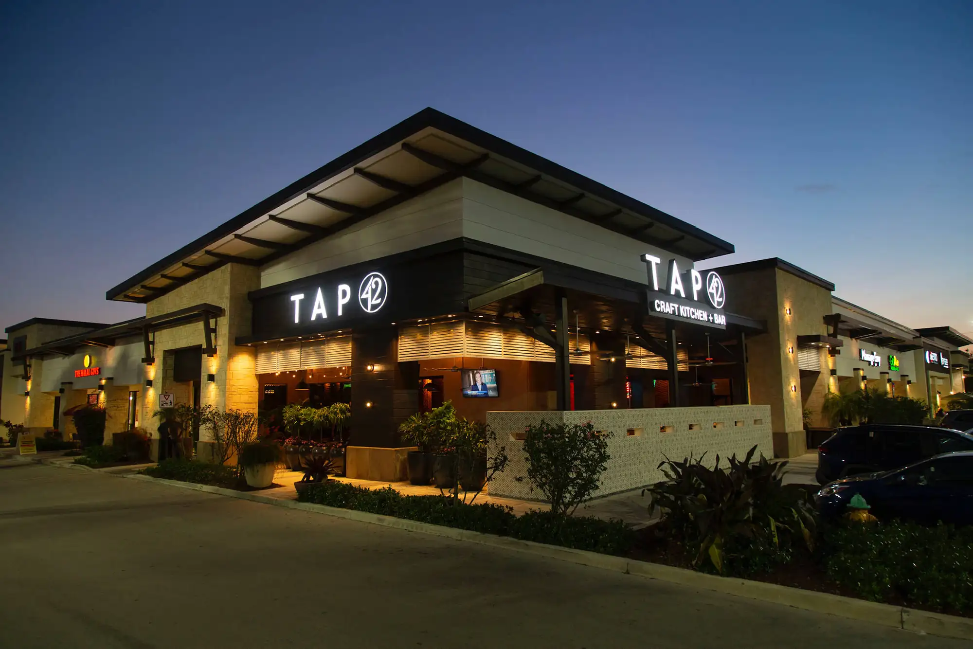 Illuminated Tap 42 signs on the building exterior and covered patio entrance at dusk at Tap 42 Davie