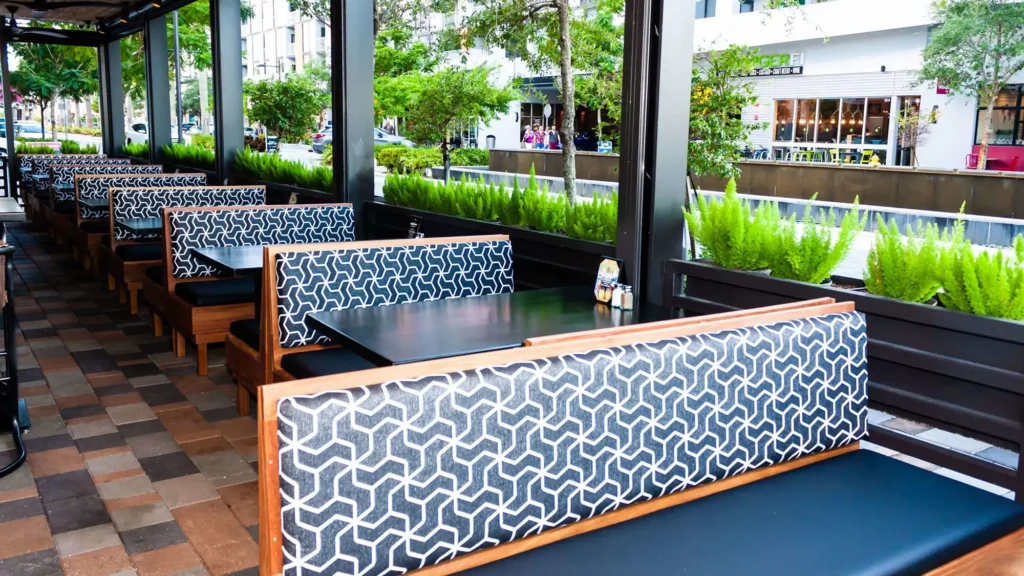 Outdoor patio booths with geometric black-and-white upholstery and fern planters at Tap 42 Doral