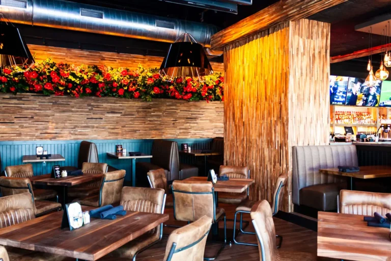 Dining room with leather chairs, wood tables, red floral wall and wood-clad column at Tap 42 Doral