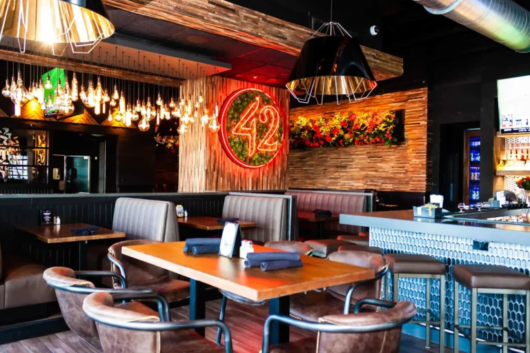 Booth seating under a cluster of hanging Edison bulbs with neon 42 sign and flower wall at Tap 42 Doral